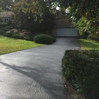 dried sealcoated driveway. driveway is surrounded by greenery and a home