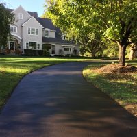 a sealcoated driveway leading back to a taupe, luxurious home